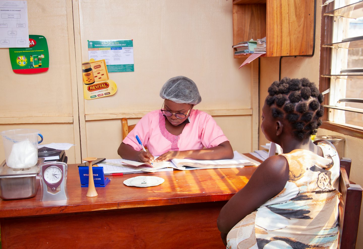 Professional in pink uniform writing in ledger at wooden desk.